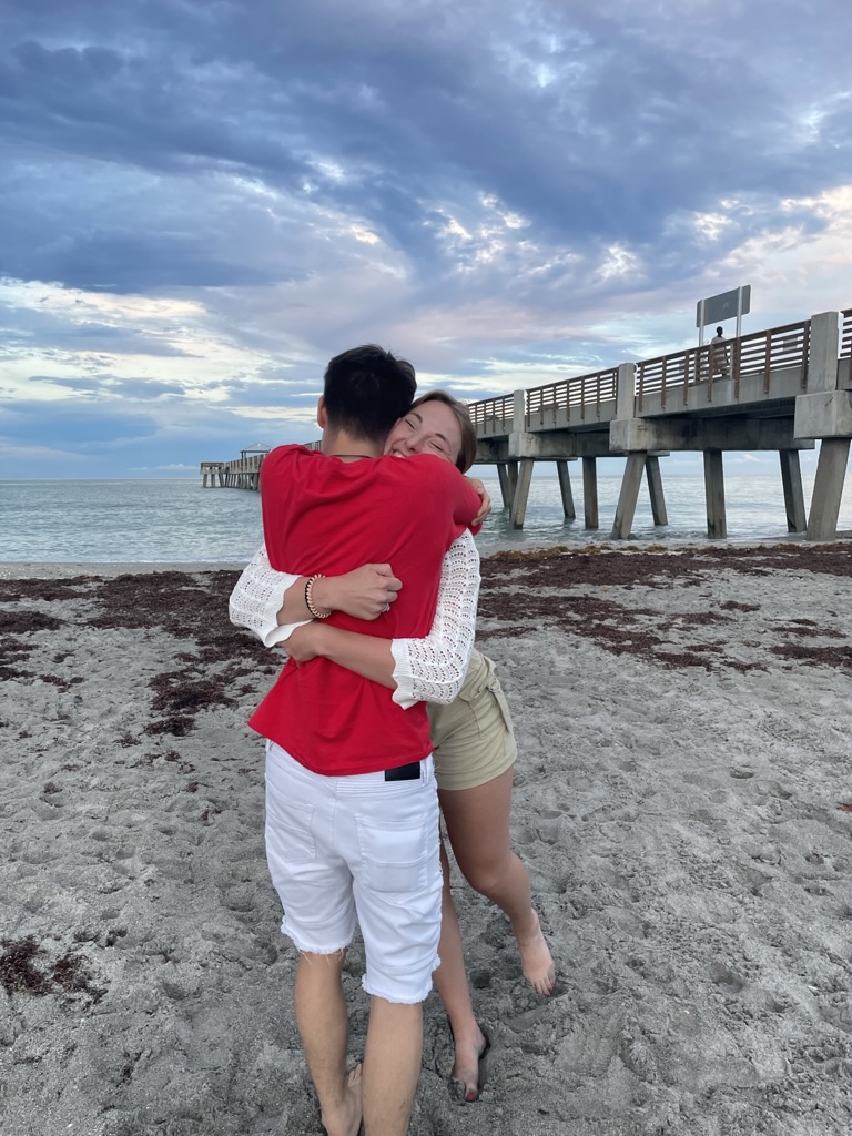 Jade and Juan hugging on the beach near a pier