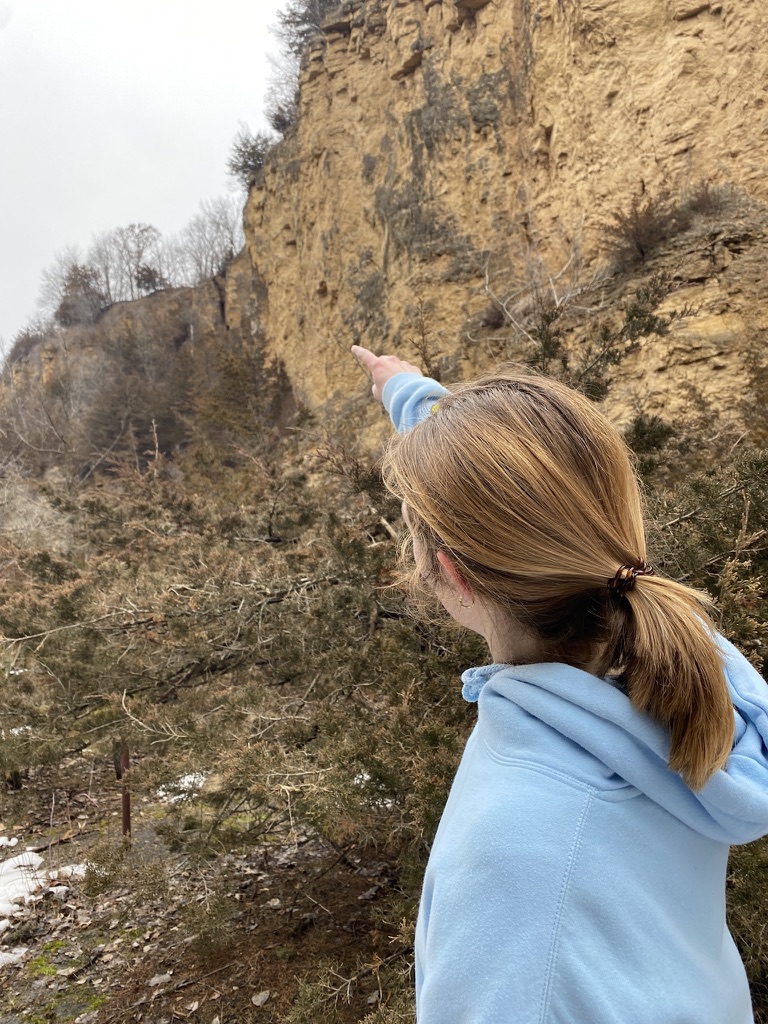 Jade pointing toward a rocky cliff during a hike