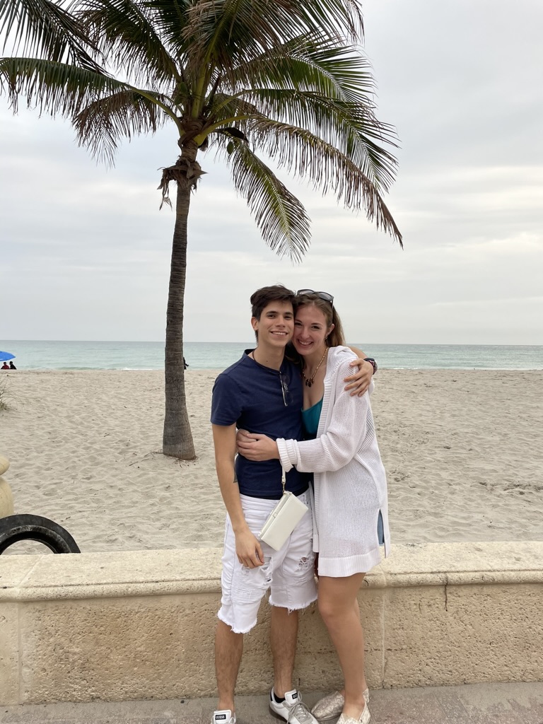 Jade and Juan hugging beneath a palm tree by the ocean