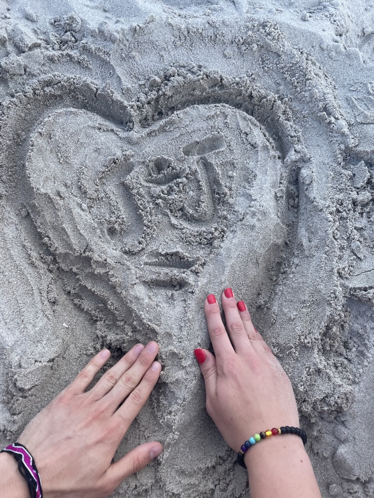 Jade and Juan’s hands beside a heart drawn in the sand